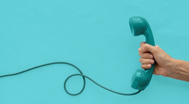 Foto un auricular de teléfono de marcación vintage azul-verde con una mano y fondo azul-verde.