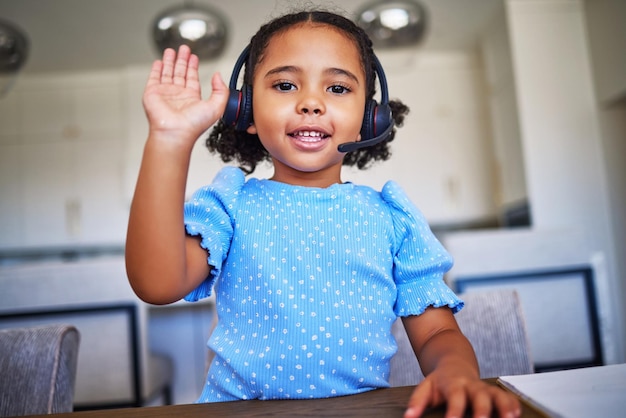 Auriculares de aprendizaje electrónico y niña haciendo una clase en línea saludando con la mano para saludar en una videollamada por Internet Comunicación feliz y retrato de un niño con aprendizaje a distancia para la educación con auriculares