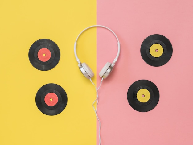 Auriculares blancos en el borde de fondo rosa y amarillo y cuatro discos de vinilo Técnica retro para reproducir música