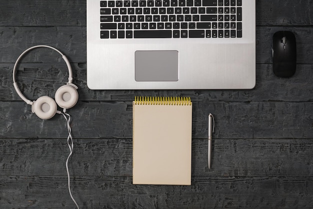 Auriculares blancos con un cable, una computadora portátil y un cuaderno sobre una mesa de madera. Accesorios para estudio, negocios y trabajo.