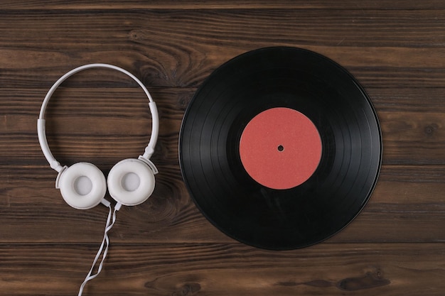 Auriculares blancos y un disco de vinilo sobre un fondo de madera