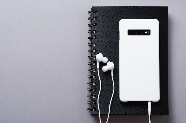 Auriculares blancos modernos, un bloc de notas para notas y un teléfono móvil sobre un fondo gris. Estilo minimalista. Vista superior con espacio de copia.