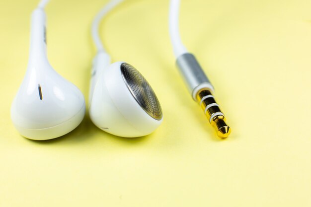 Auriculares blancos sobre fondo amarillo. Concepto de música moderna. Tecnología de audio. Cerca de la foto.