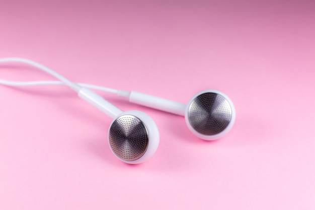 Auriculares blancos sobre fondo rosa. Concepto de música moderna. Tecnología de audio. Cerca de la foto.