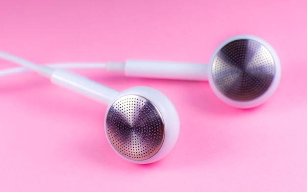 Auriculares blancos sobre fondo rosa. Concepto de música moderna. Tecnología de audio. Cerca de la foto.