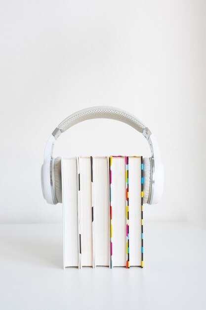 Auriculares blancos sobre una pila de 5 libros sobre una mesa sobre una pared blanca de fondo. concepto de audiolibro. copie el espacio.