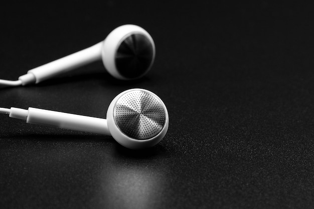 Auriculares blancos en textura negra con sombra