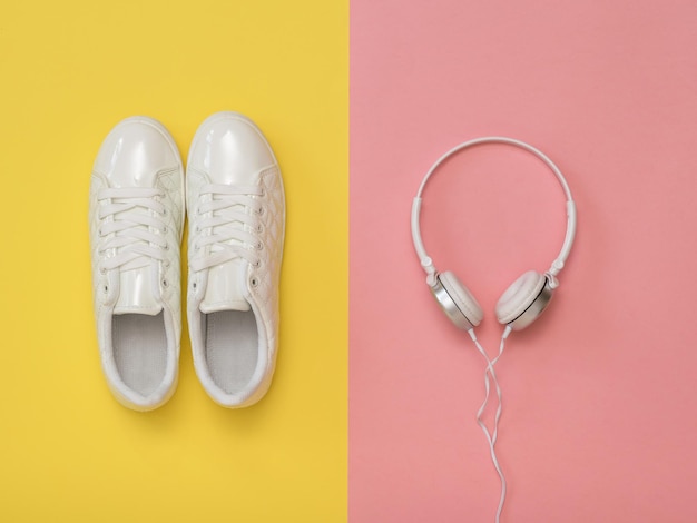Auriculares blancos y zapatillas blancas sobre un fondo rosa y amarillo. El concepto de un estilo de vida saludable y música.
