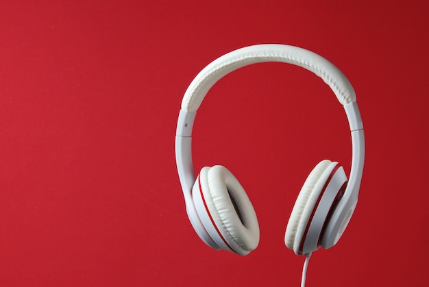 Auriculares con cable clásicos blancos aislados sobre fondo rojo. Estilo retro. Concepto de música minimalista.