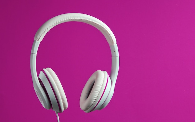 Auriculares con cable clásicos blancos aislados sobre fondo rosa. Estilo retro. Concepto de música minimalista.