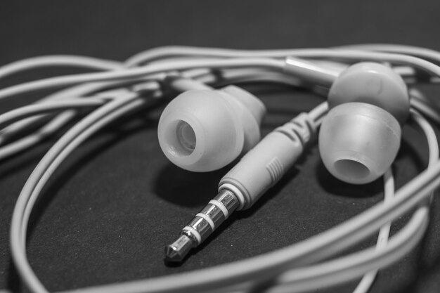 Auriculares con cable trenzado blanco sobre una superficie negra monocromática, primer plano. Auriculares para un teléfono móvil. Música.