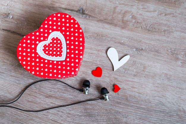 Auriculares y una caja de regalo en forma de corazón y corazones pequeños sobre un fondo de madera Concepto de regalo de música Vista superior con espacio de copia