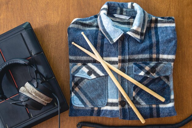 Auriculares y camisa a cuadros doblada y baquetas sobre un fondo de madera