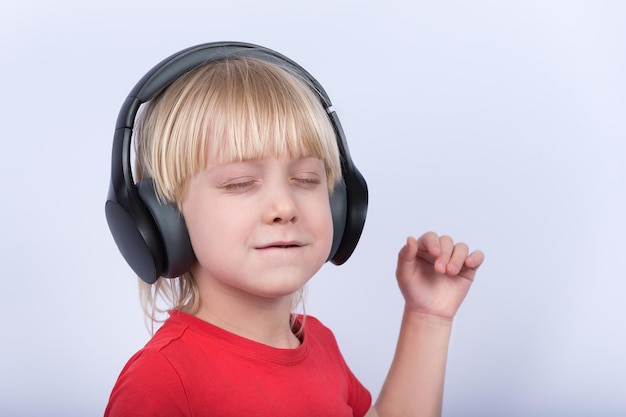 Auriculares de chico rubio con placer de escuchar música. Retrato de niños con auriculares sobre fondo blanco.