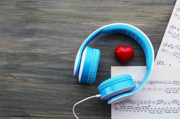 Auriculares con corazón rojo y notas musicales en la mesa de madera de cerca