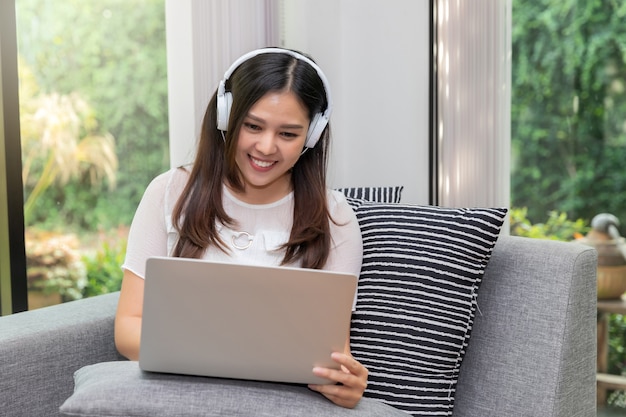 Auriculares del desgaste de mujer que se sientan en el sofá y que usan en la tableta.