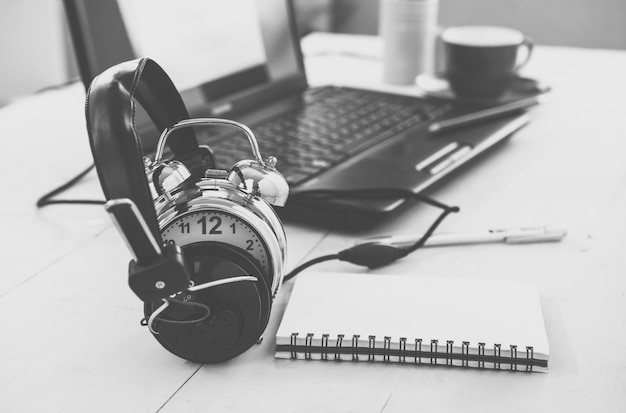 Auriculares y despertador en la mesa de trabajo. Concepto de educación o relax. Tono vintage, efecto de filtro retro.