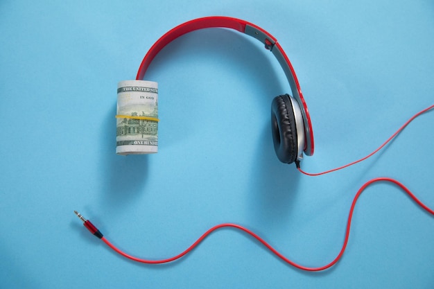 Auriculares con un dólar en el fondo azul.