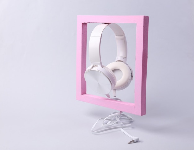 Auriculares estéreo blancos con marco rosa sobre fondo gris Bodegón musical minimalista moderno