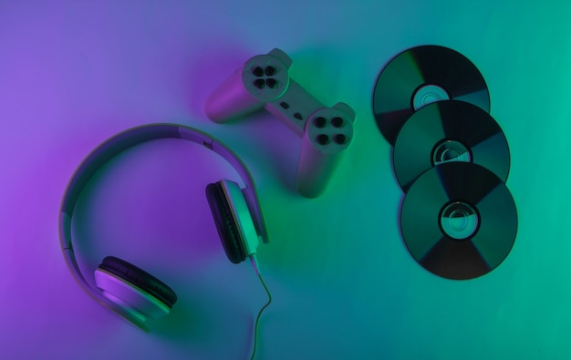 Auriculares estéreo con gamepad retro y discos cd. Luz neón púrpura y verde. Concepto de juego