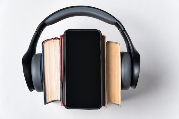 Auriculares estéreo, libros y un teléfono sobre un fondo blanco. Concepto de audiolibros. Copia espacio