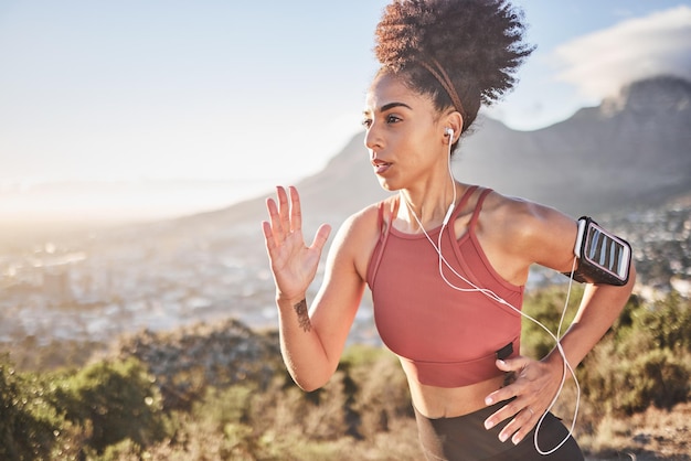 Auriculares fitness y mujer negra corriendo en la naturaleza al aire libre transmitiendo música de radio o podcast para motivar Bienestar de la salud y corredora escuchando canciones de audio y bandas sonoras de entrenamiento