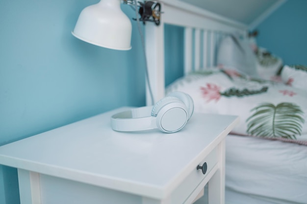 Los auriculares inalámbricos blancos se encuentran en la mesita de noche cerca de la cama en la habitación del hotel