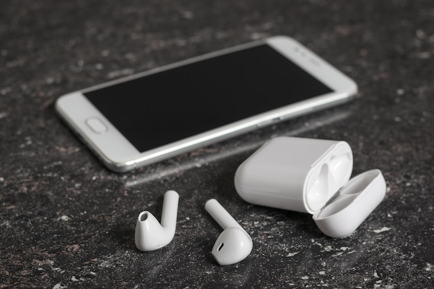 Auriculares inalámbricos blancos y un teléfono inteligente blanco sobre un fondo de piedra. Accesorios inalámbricos modernos.