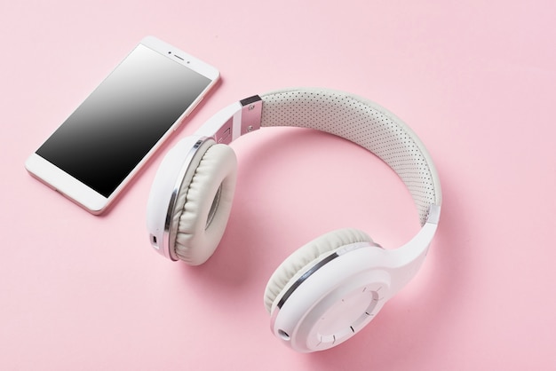 Auriculares inalámbricos blancos y teléfono inteligente en rosa pastel.