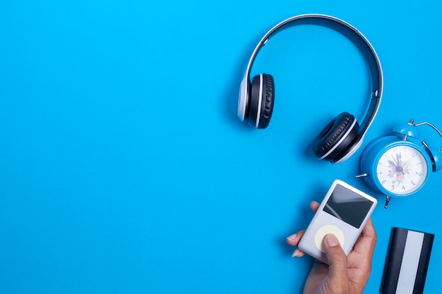 Auriculares inalámbricos y reproductor multimedia, reloj despertador azul sobre fondo de papel azul