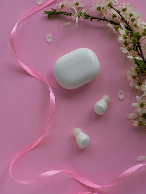 Auriculares inalámbricos sobre fondo rosa con flores de cerezo y espacio de copia