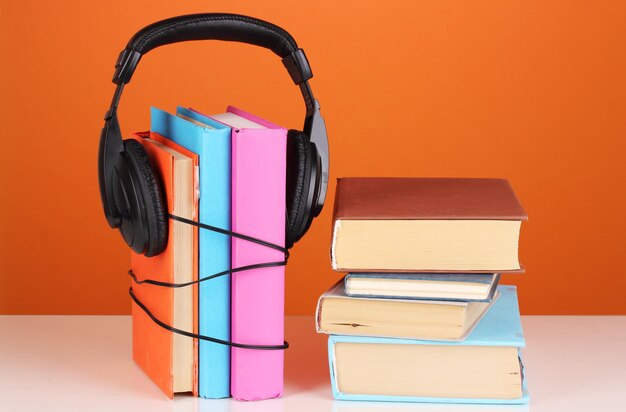 Auriculares en libros sobre fondo naranja