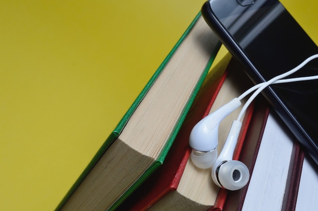 Auriculares con libros y un teléfono inteligente sobre un fondo amarillo.