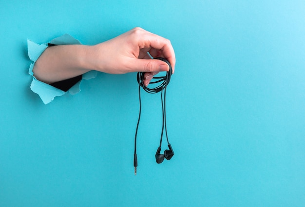 Auriculares en la mano de una mujer sobre un fondo azul con un agujero