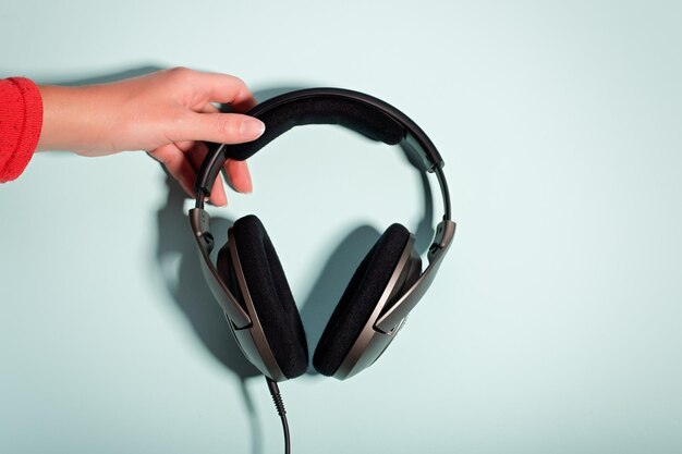 Foto auriculares masivos negros en mano femenina sobre espacio de copia de fondo pastel