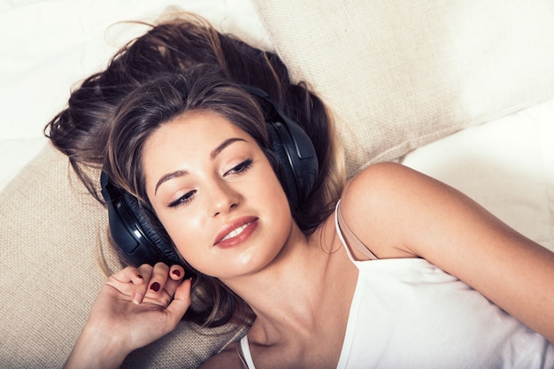 Auriculares de mujer hermosa joven escuchando música en la cama