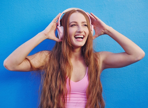 Auriculares de música y fondo azul con una mujer transmitiendo o escuchando audio por diversión Radio internet y 5g con una atractiva joven usando tecnología inalámbrica para escuchar una canción