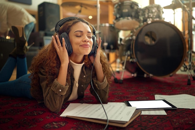 Foto auriculares de música y mujer en el estudio transmitiendo una canción de podcast o radio en línea meditación relajante y una artista negra escuchando una grabación de audio mientras está acostada en el suelo con una tableta de maqueta