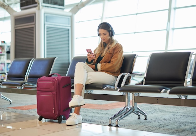 Auriculares música teléfono y mujer en el vestíbulo del aeropuerto en redes sociales navegación por Internet o desplazamiento web Tecnología móvil de vuelo de viaje y mujer con aplicación de teléfono inteligente para transmisión de radio o podcast