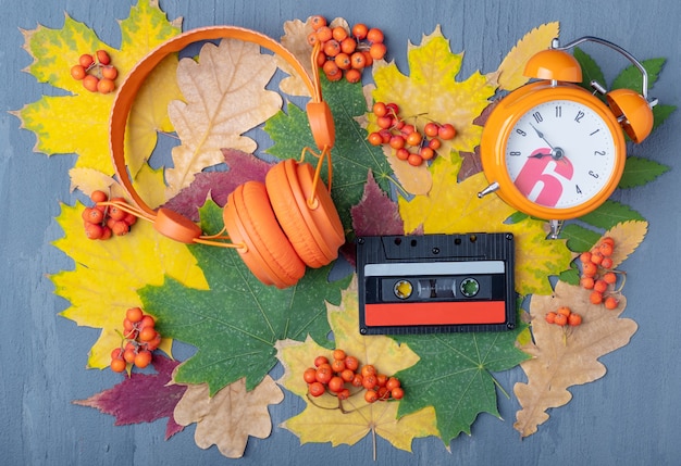 Foto auriculares naranjas, despertador y casete de audio magnético sobre un fondo azul con hojas rojas y amarillas y bayas naranjas. lista de reproducción de otoño favorita conceptual. es hora de escuchar el concepto de música.