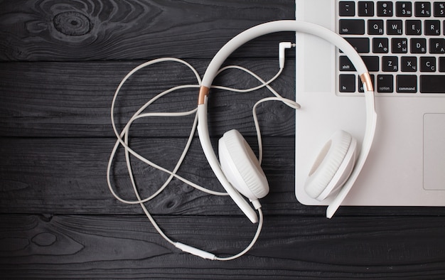 Auriculares y ordenador portátil blanco sobre fondo de madera.