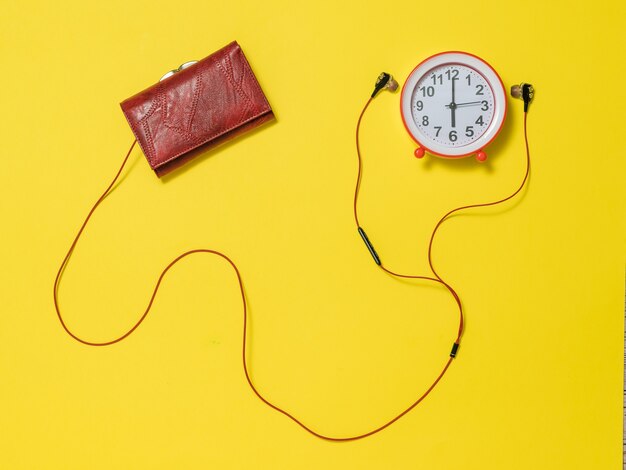 Auriculares que sobresalen de la billetera y un despertador rojo. El concepto de levantar el tono por la mañana.