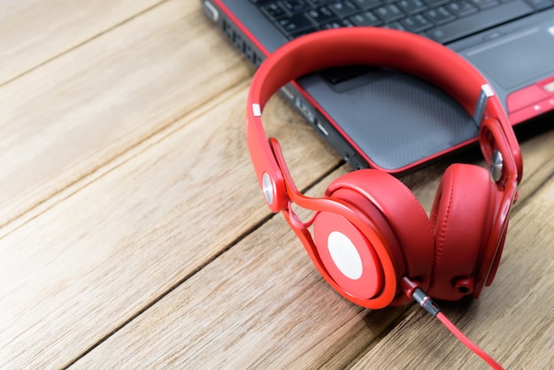 Auriculares rojos colocados en el portátil o portátil negro y en la mesa de madera