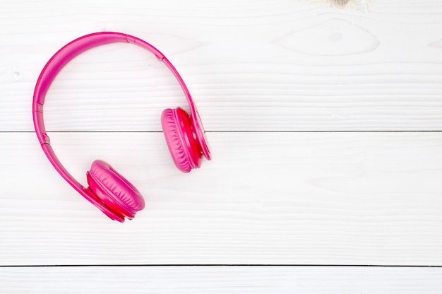 Auriculares rosa para escuchar sonido y música en una mesa de madera blanca