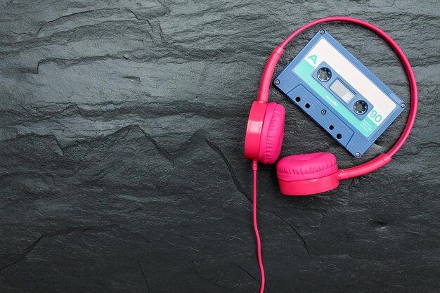 Foto auriculares rosas y cassette de audio de cinta azul sobre un fondo de piedra de pizarra húmeda