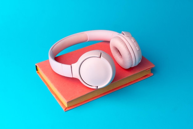 Auriculares rosas sobre un libro sobre fondo azul