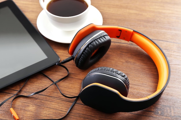 Auriculares con tableta y taza de café en la mesa de madera de cerca