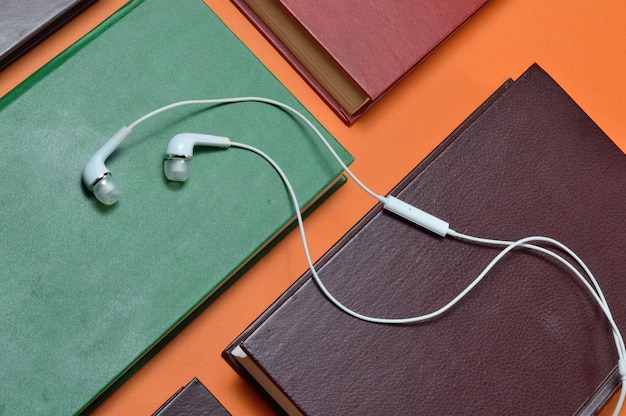 Los auriculares de vacío blancos se encuentran sobre libros dispuestos sobre un fondo naranja. concepto de audiolibro.