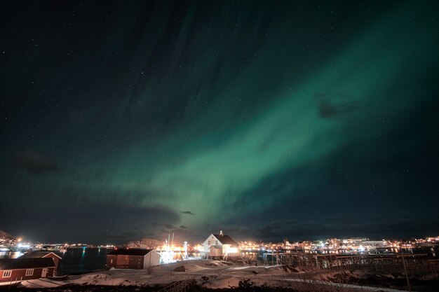 Aurora boreal, aurora boreal sobre uma vila escandinava na costa das ilhas lofoten, na noruega