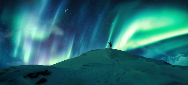 Aurora boreal brillando sobre un excursionista de silueta parado en la montaña en el cielo nocturno